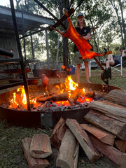 Wood being burned in a fire pit with people around an Asado
