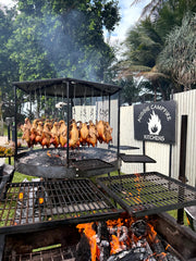 Barbecue grill with food being cooked outdoors, featuring a brand logo on a sign.