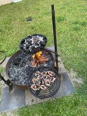 Outdoor cooking setup with a fire pit and cast iron skillets on a grassy area.