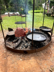 Outdoor cooking setup with pots over a fire pit in a backyard.