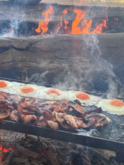 BBQ cooking on a folding hot plate outdoors with visible flames and smoke.