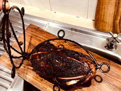 Smoked meat on a wooden cutting board with a decorative metal holder in a kitchen setting.