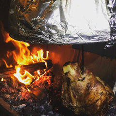 Food being cooked using the Bell Oven Kit, which is placed over an open fire, with foil wrapped around the food for smoking.